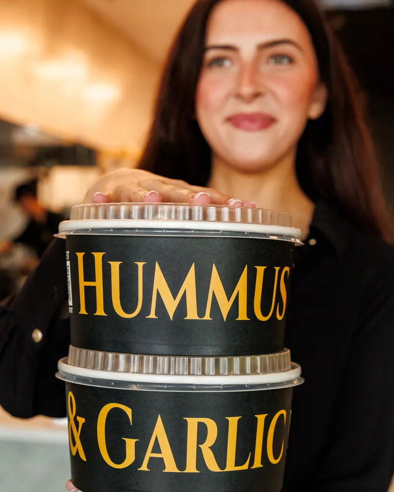 A team member carrying two stacked Hummus & Garlic catering bowls