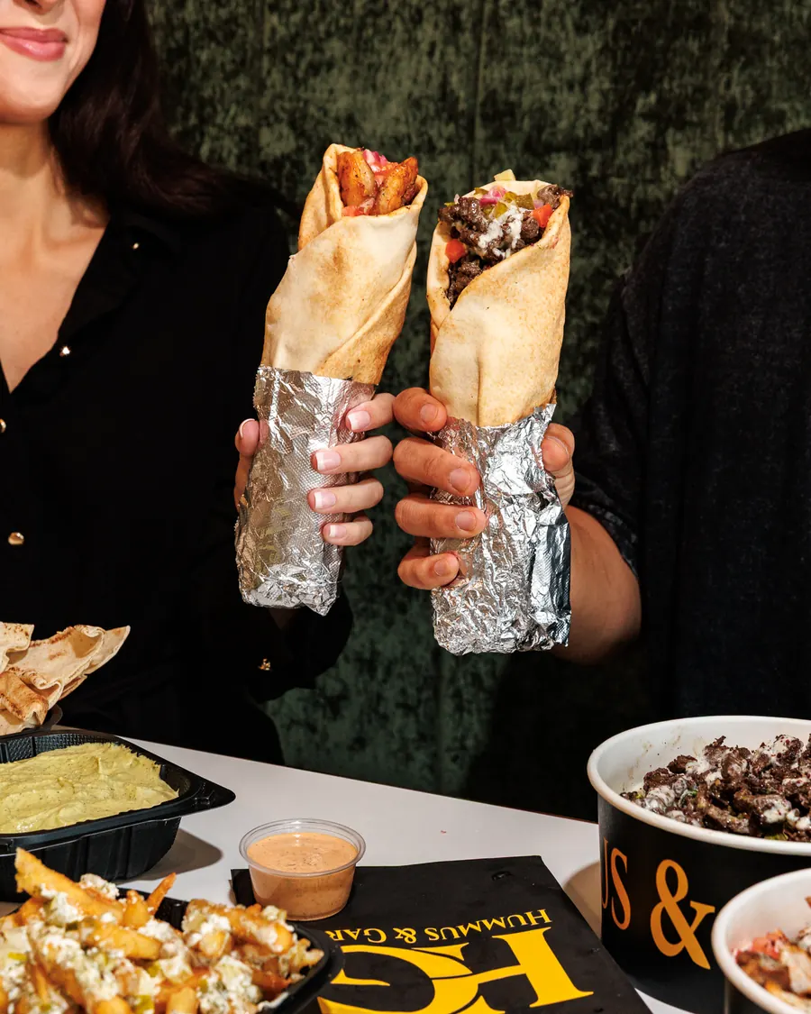 Two guests holding up chicken and steak shawarma wraps in foil