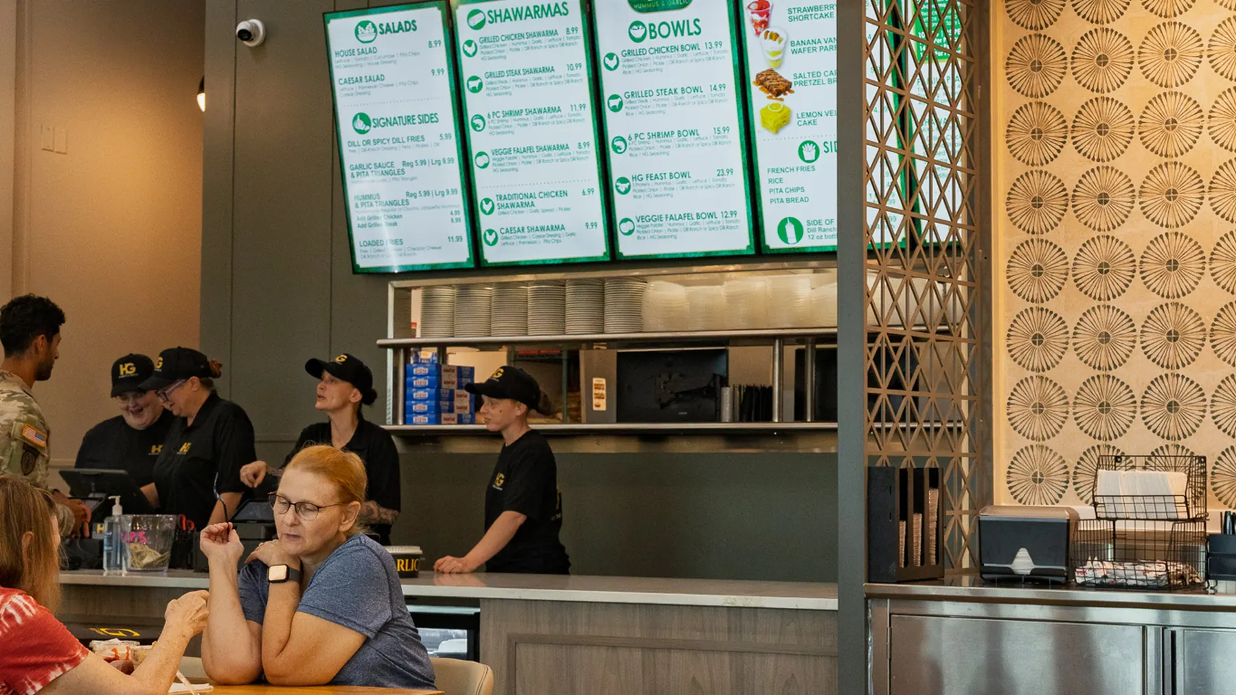 Guests eating at tables inside Hummus & Garlic with the menu boards behind the counter