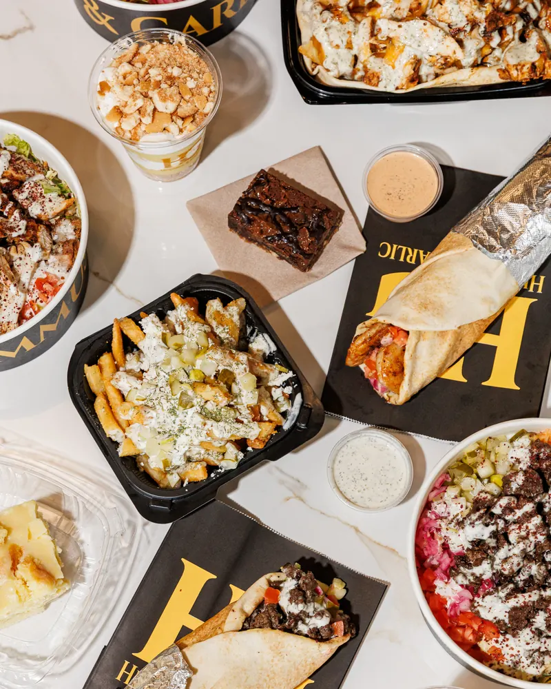 Overhead spread of loaded fries, a shawarma wrap, a brownie, sauces and a bowl