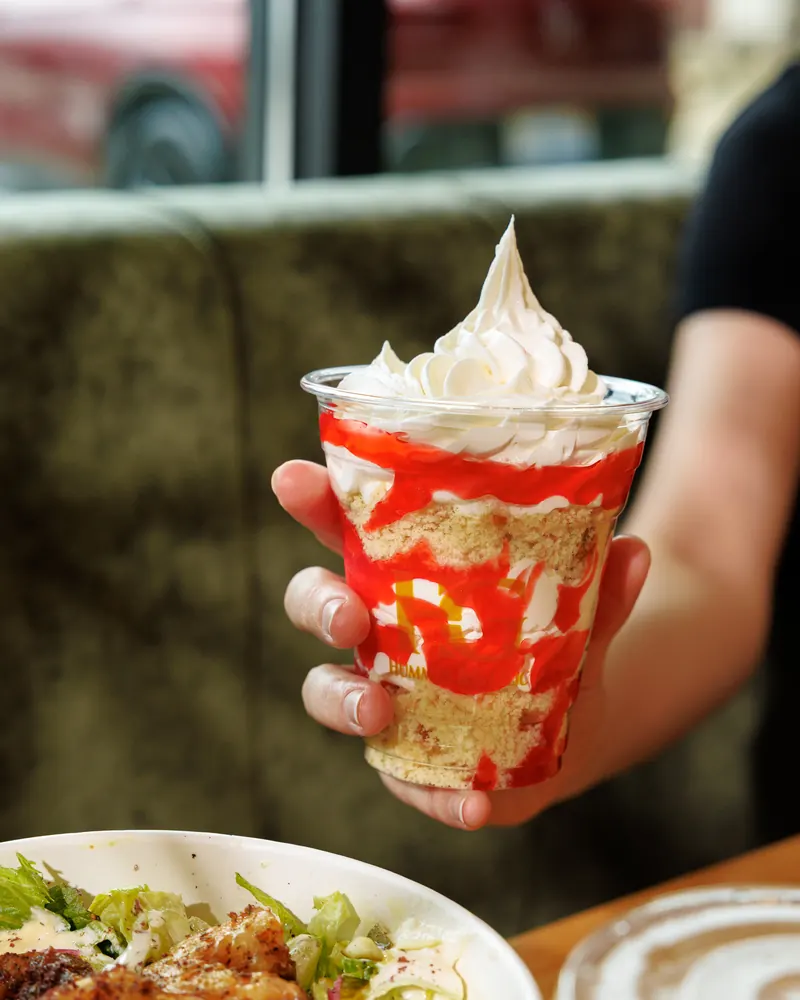 A guest holding a strawberry shortcake parfait over a shrimp bowl