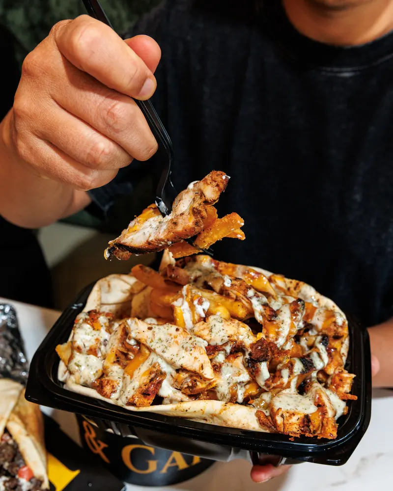 A guest lifting a forkful of loaded shawarma fries