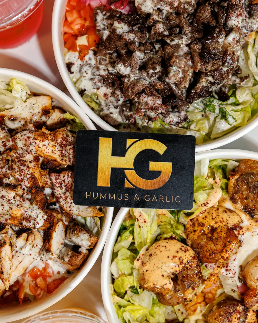 A black and gold Hummus & Garlic gift card resting on three loaded bowls
