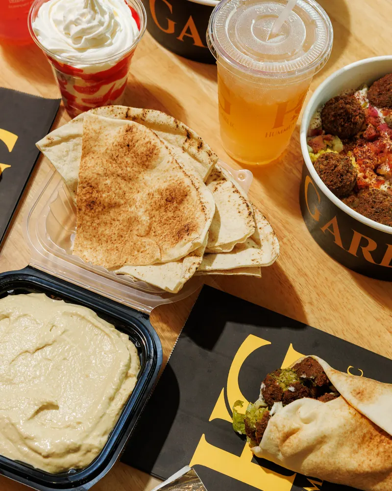 Warm pita, a tray of hummus, a shawarma and bowls shared across the table